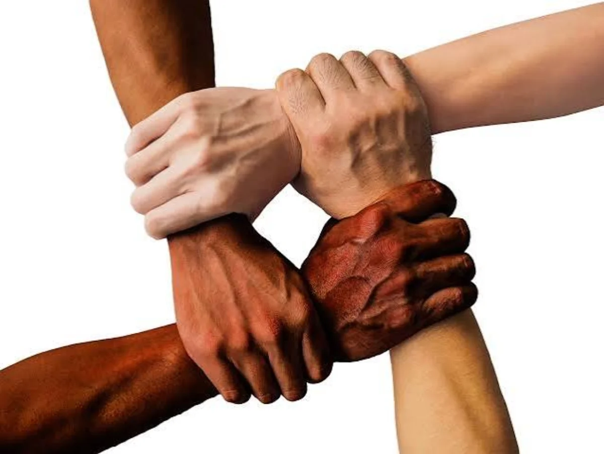 Entraide locale : quatre mains de teints divers qui se saisissent les poignets en cercle, symbole de solidarité.